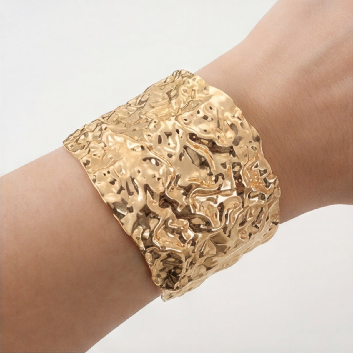 Wide gold-tone raised-texture cuff bracelet worn on the wrist