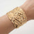 Wide gold-tone raised-texture cuff bracelet worn on the wrist
