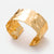 Wide gold-tone hammered open cuff bracelet shown at an angle