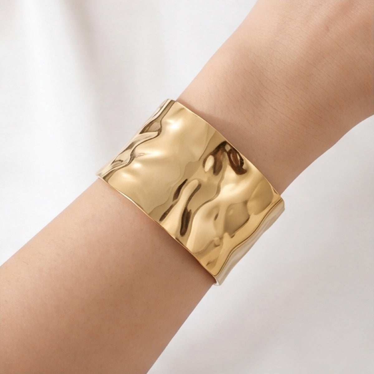 Wide gold-tone hammered cuff bracelet worn on the wrist