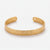 Front-facing detail of the slim gold-tone textured open cuff bracelet