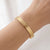 Slim gold-tone textured cuff bracelet worn on the wrist